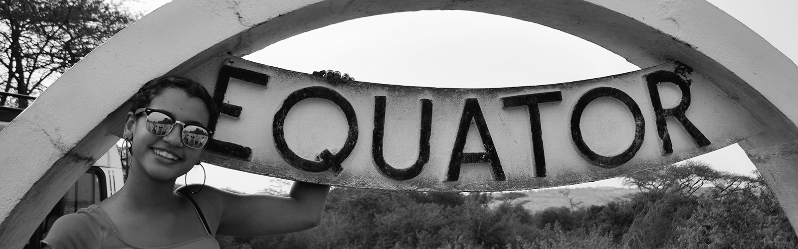 A student posed next to a curved sign that reads "EQUATOR".